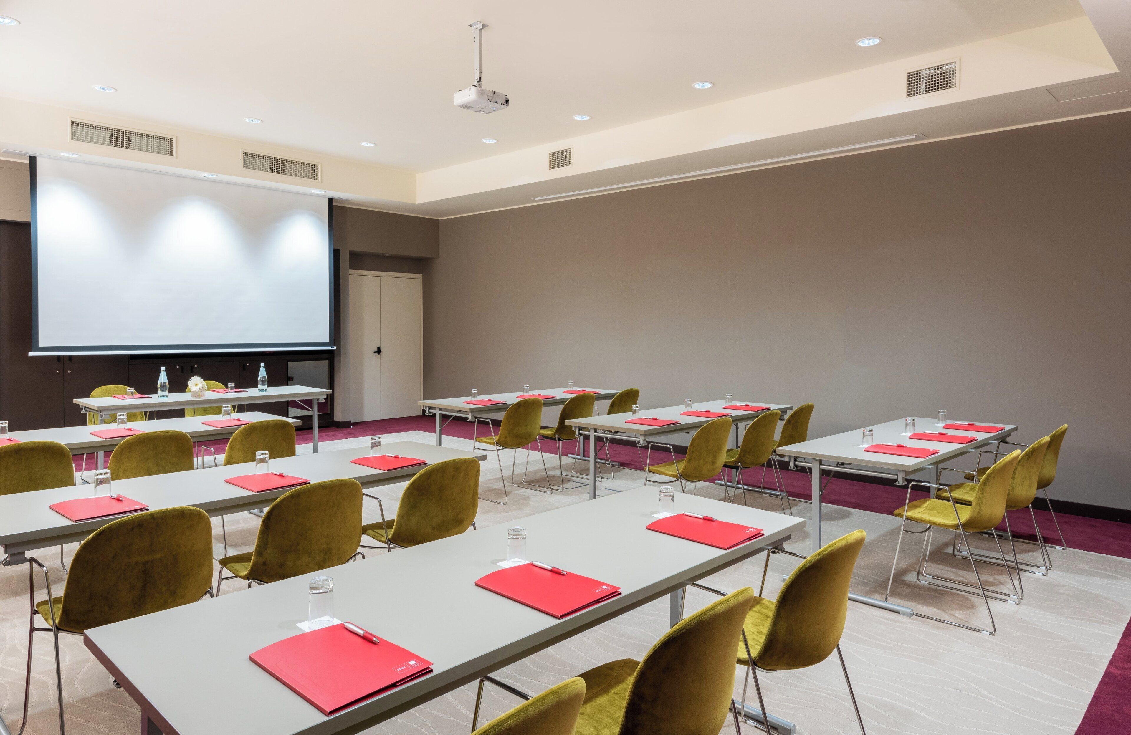 A conference room with multiple tables, yellow chairs, and a large screen.