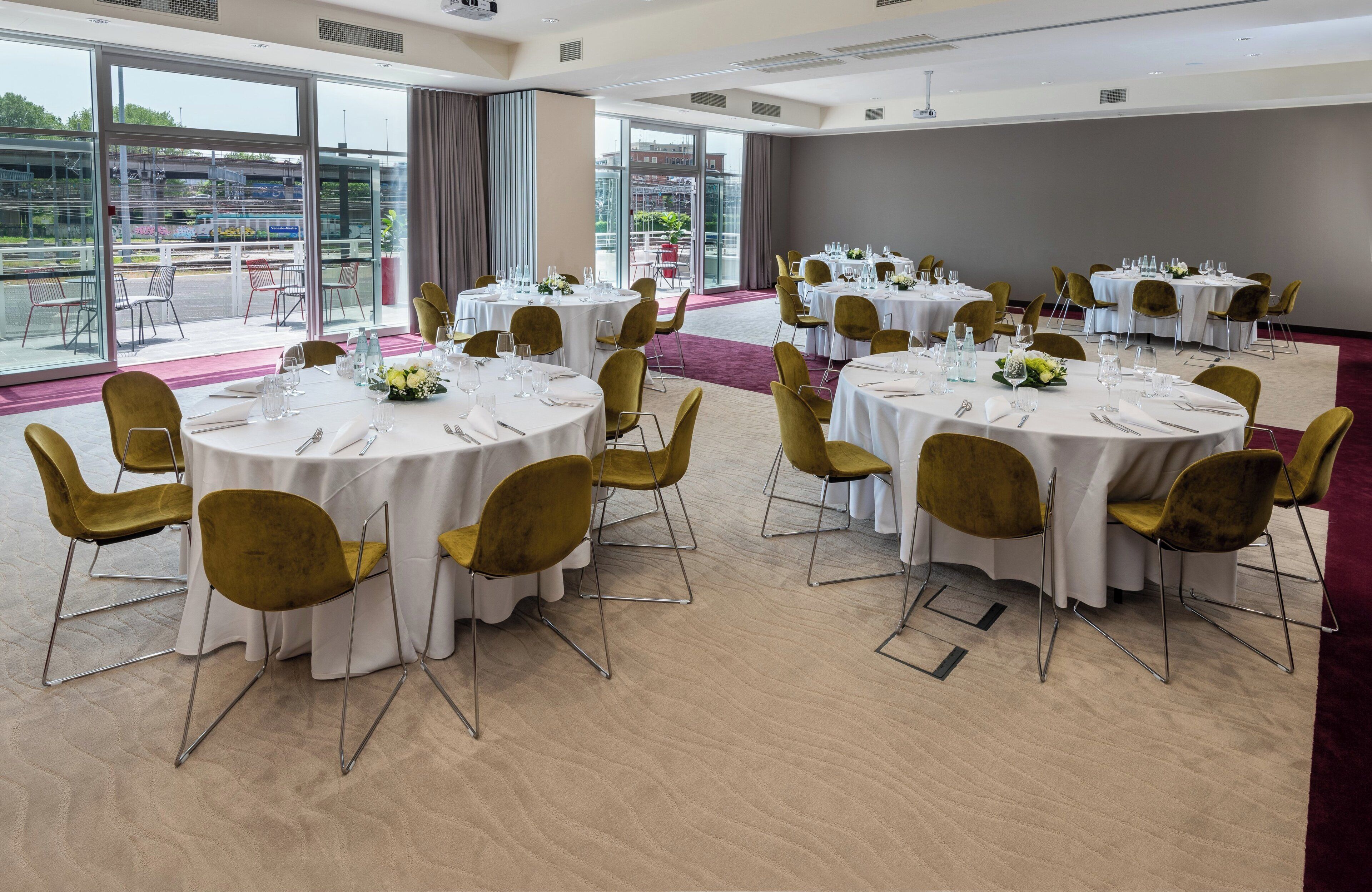 A conference room with round tables, gold chairs, and large windows offering a view of the outside.