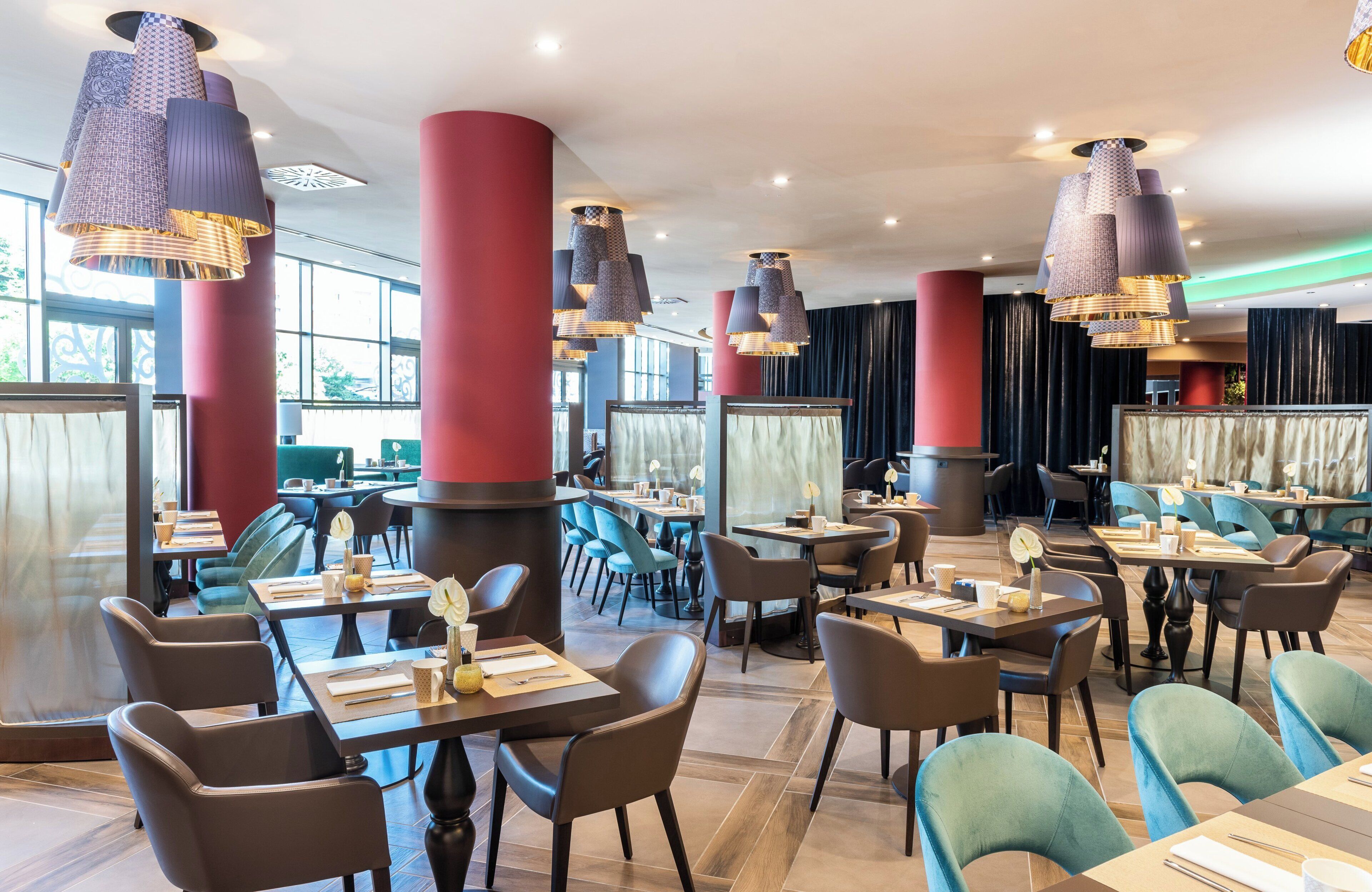 Un restaurant modern amb sostres alts, pilars vermells i nombroses taules i cadires.