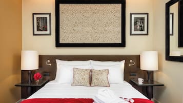 A neatly made bed with white linens and red accents, two bedside tables with lamps, and framed artwork on the walls.