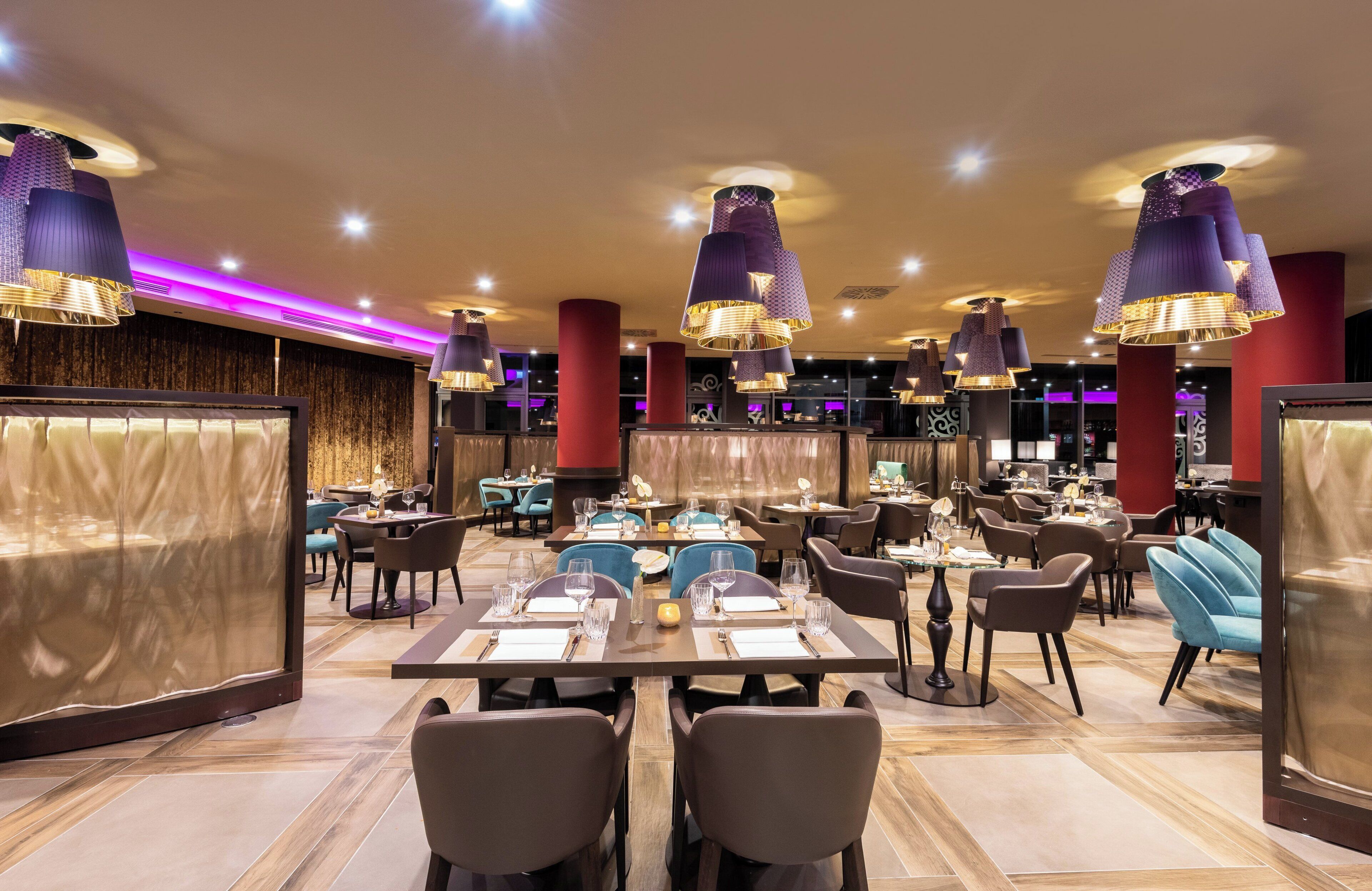 A restaurant with multiple tables and chairs, purple hanging lamps, and a modern interior design.