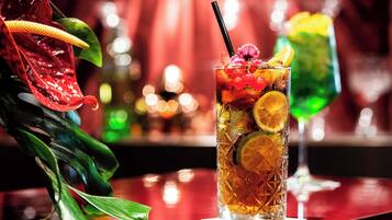 A tall glass with a straw, garnished with fruit and a flower, placed on a reflective surface with a blurred background.