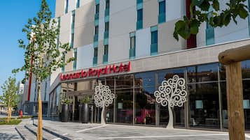El exterior del Hotel Leonardo Royal, con fachada moderna, amplios ventanales de vidrio y esculturas de árboles decorativas en la entrada.