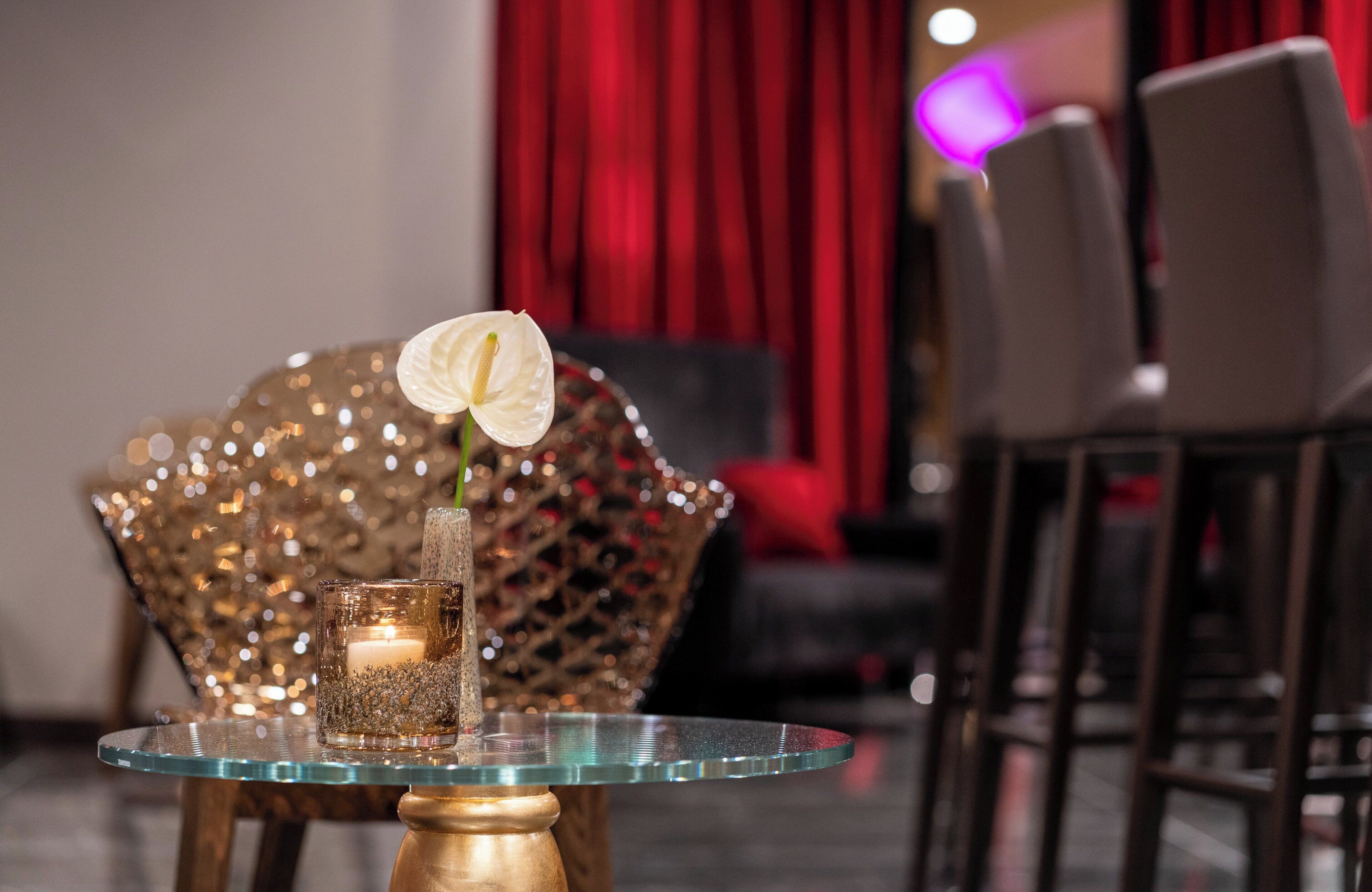 Une table en verre ornée d’une bougie et d’une fleur blanche, le tout placé devant un rideau rouge.