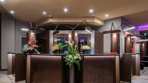 Zona de recepción con diseño moderno, que incluye un mostrador de recepción, múltiples lámparas colgantes y arreglos florales.