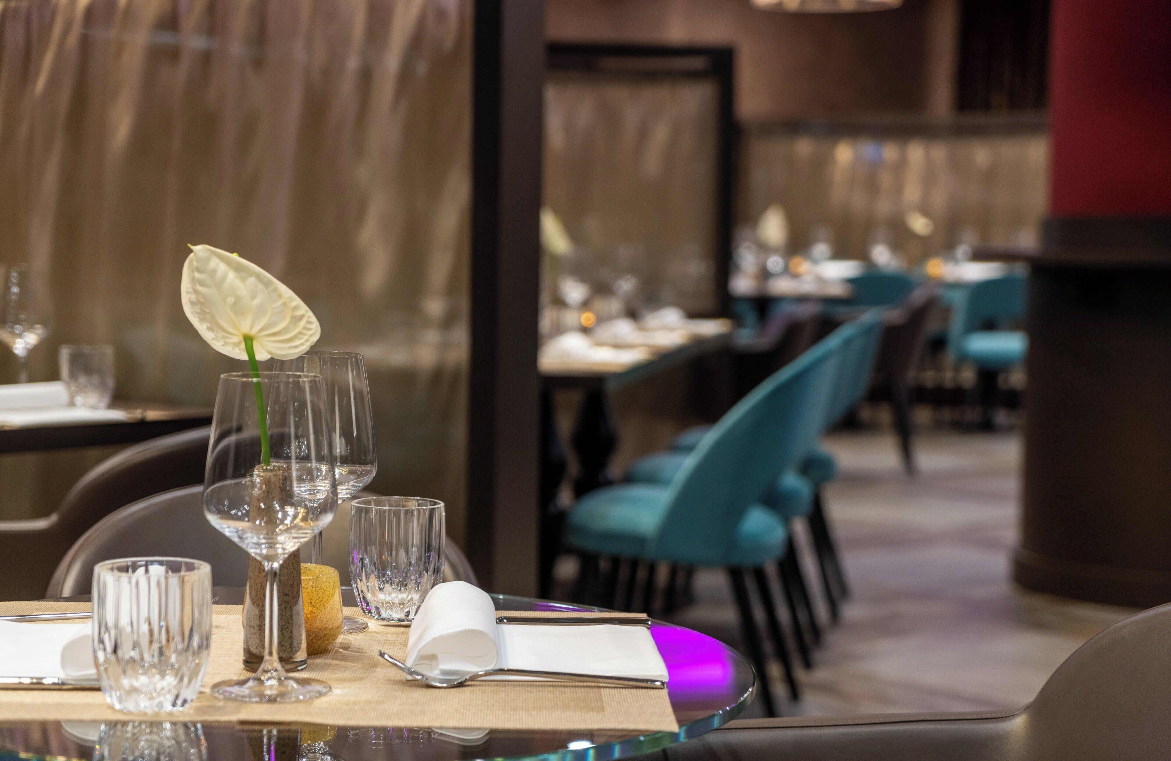A restaurant interior with tables set for dining, featuring clear glassware and a decorative flower.
