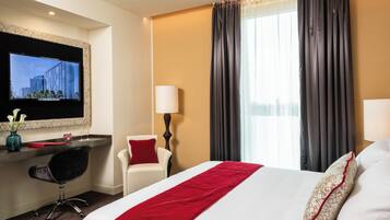 A hotel room with a bed, a desk with a chair, a TV, and a window with curtains.