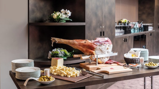 Montaje de bufé con un gran jamón asado, queso, aceitunas y diferentes condimentos.