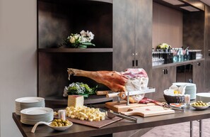 Een buffetopstelling met een groot gebraden varkensschouder, kaas, olijven en diverse sauzen.