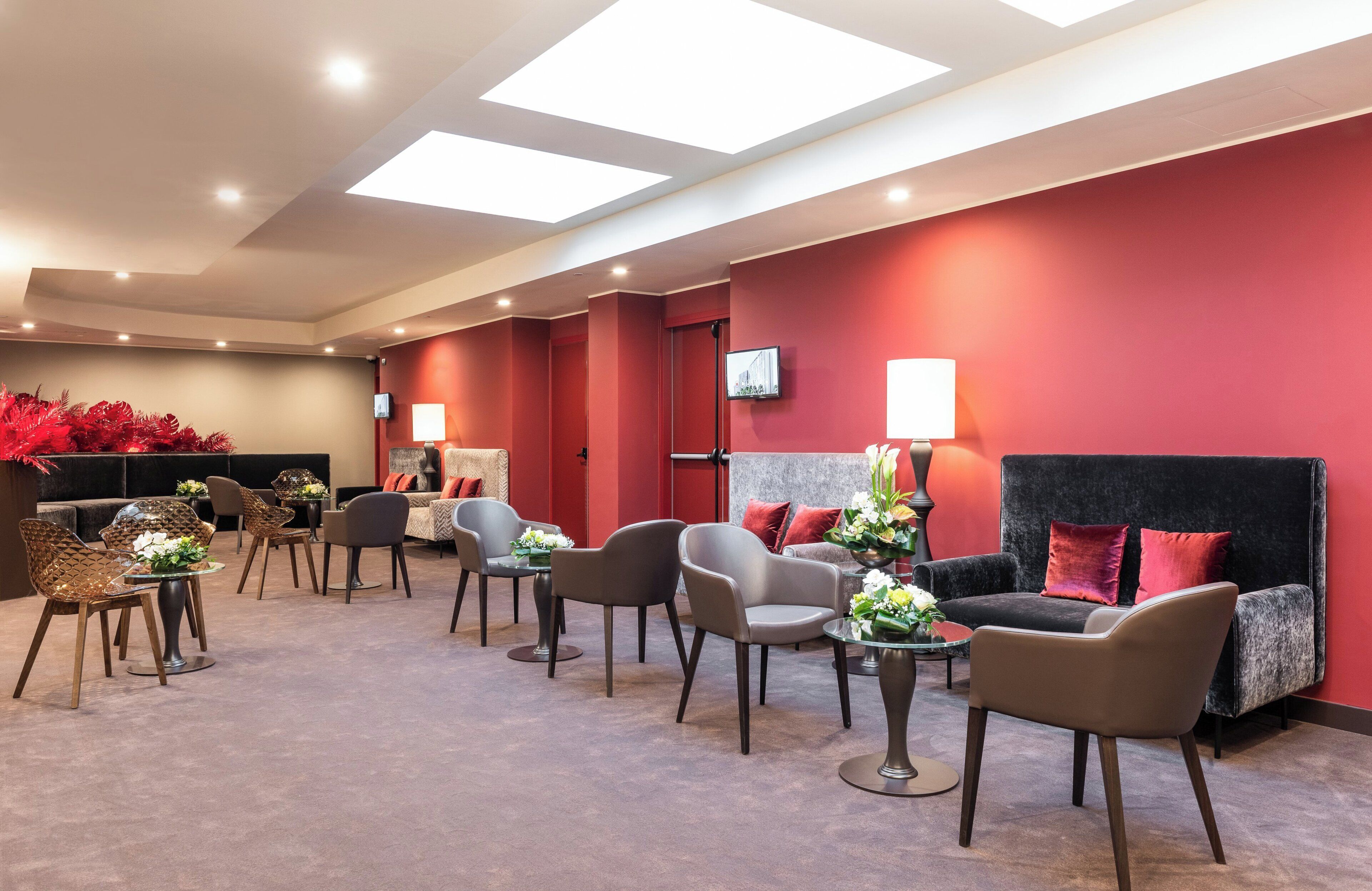 A modern hotel lobby with a red accent wall, comfortable seating, and a flat-screen TV mounted on the wall.