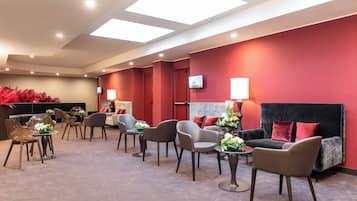 A modern hotel lobby with a red accent wall, comfortable seating, and a flat-screen TV mounted on the wall.