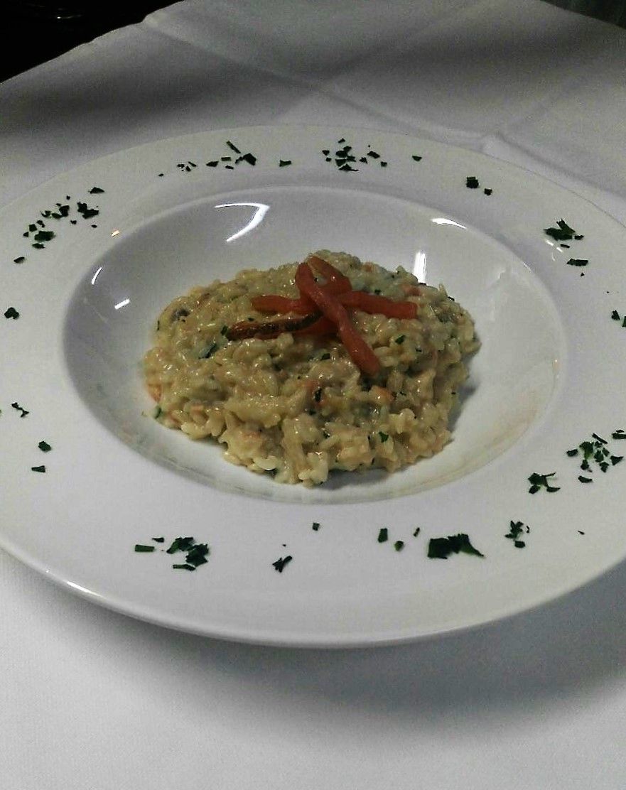 A plate of risotto with a garnish of red pepper and herbs, served on a white plate with a simple design.
