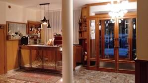 A hotel lobby with a bar area, a large pillar, and a glass door leading outside. - Hotel Viola (Caramanico Terme)