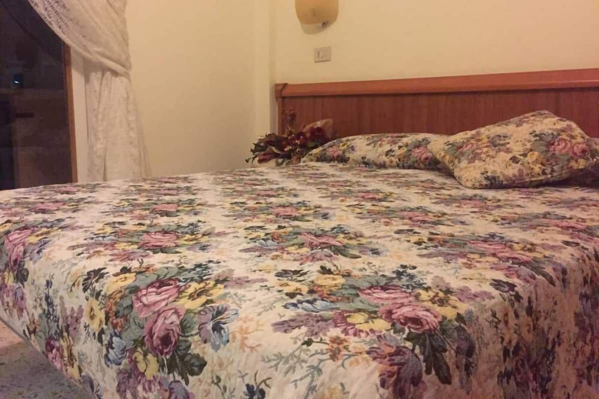 A bedroom with a floral bedspread, a wooden headboard, and a wall-mounted light fixture.