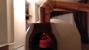 A wood-fired pizza oven with a copper chimney, located in a kitchen with a marble countertop and a window with curtains. - Hotel Viola (Caramanico Terme)