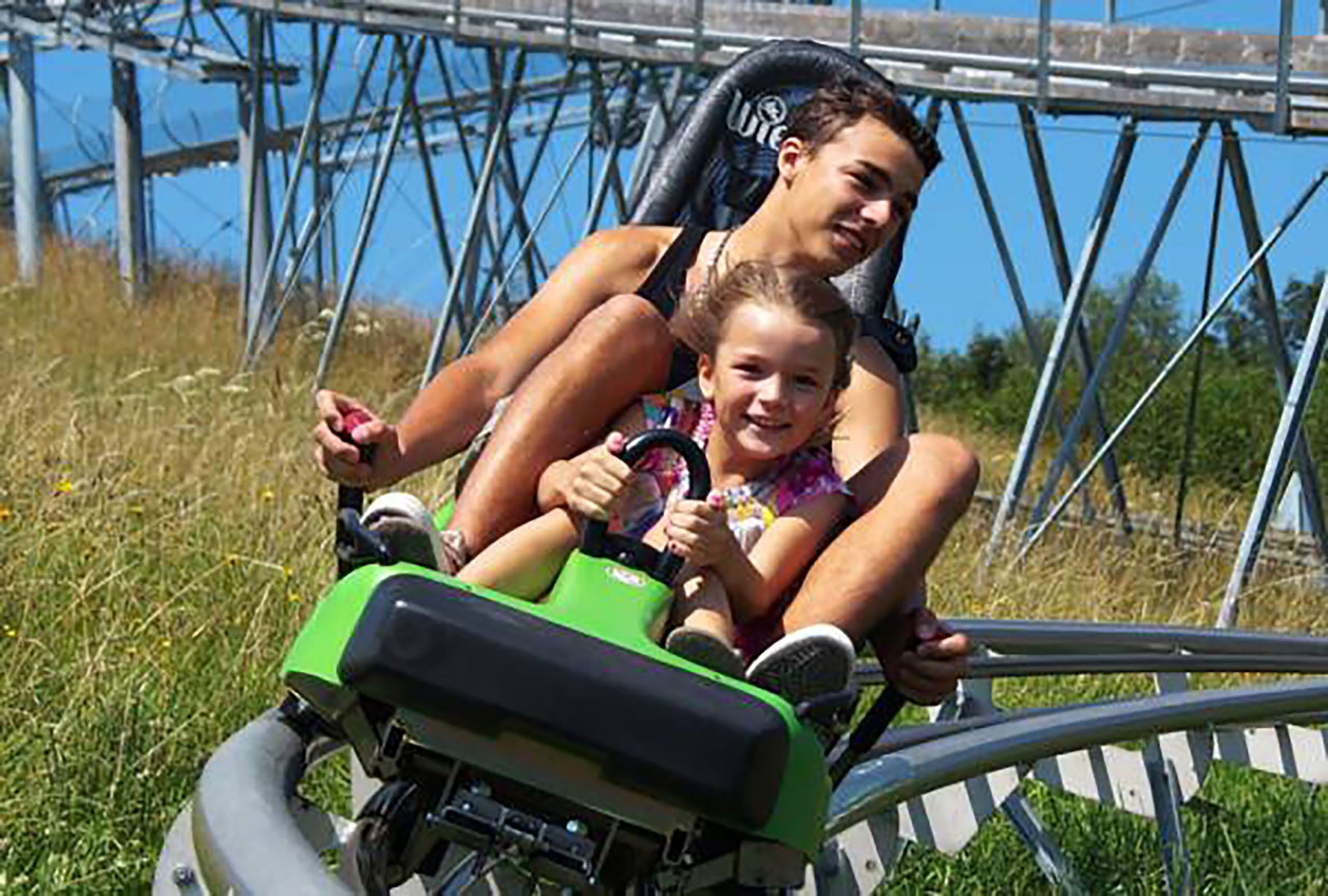 A person riding a green and black vehicle on a track with metal railings and a clear blue sky in the background.