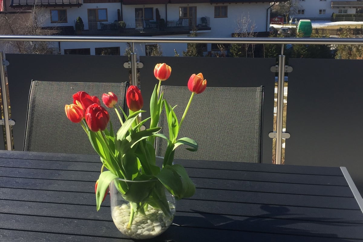 Een tafel met een vaas tulpen, een stoel en een uitzicht op besneeuwde bergen en huizen op de achtergrond.
