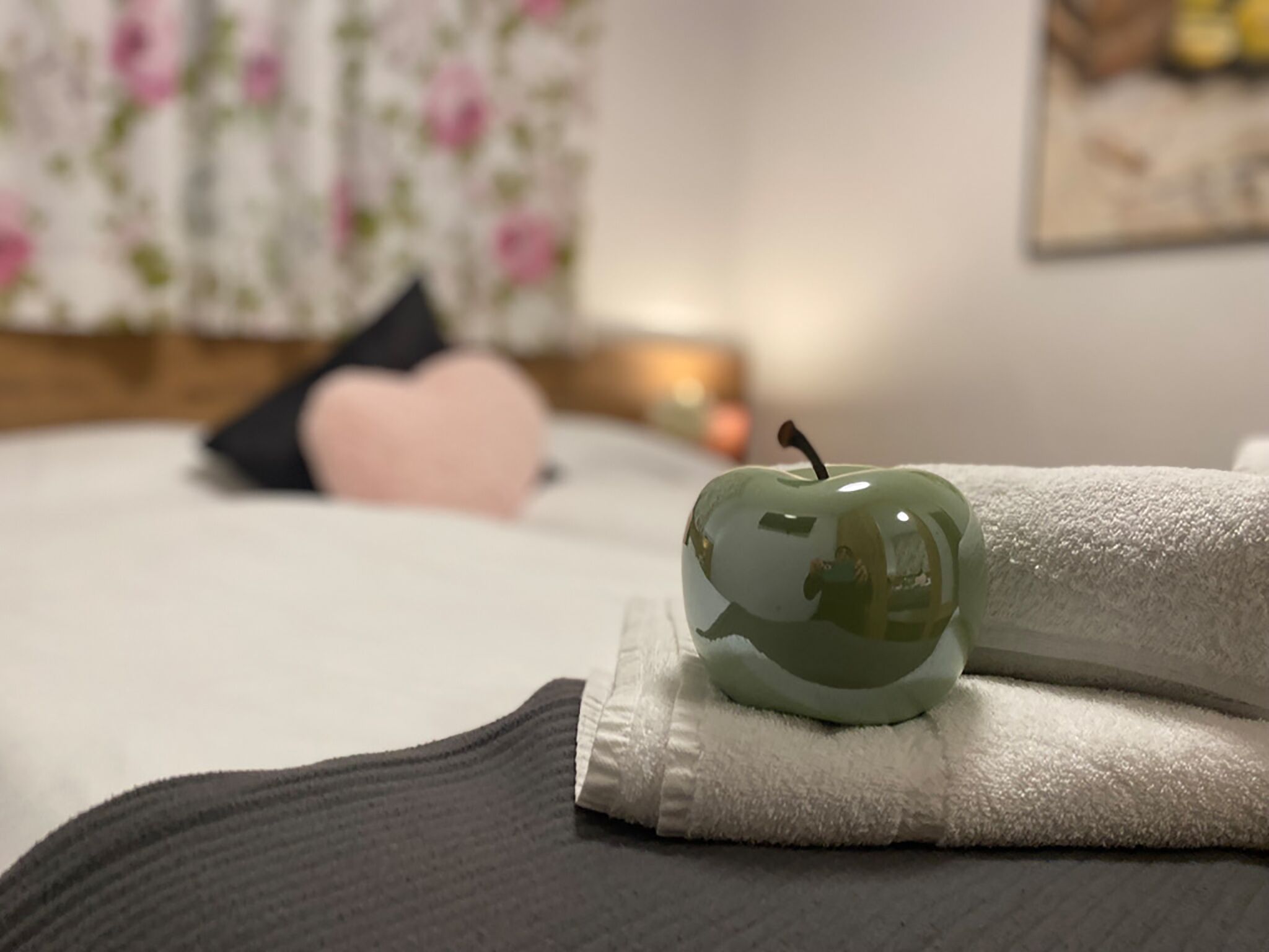 Une bougie en forme de pomme verte, posée sur un lit avec un oreiller blanc et une couverture grise.