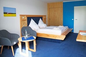 A room with a bed, a chair, a small table, and a wooden wardrobe.