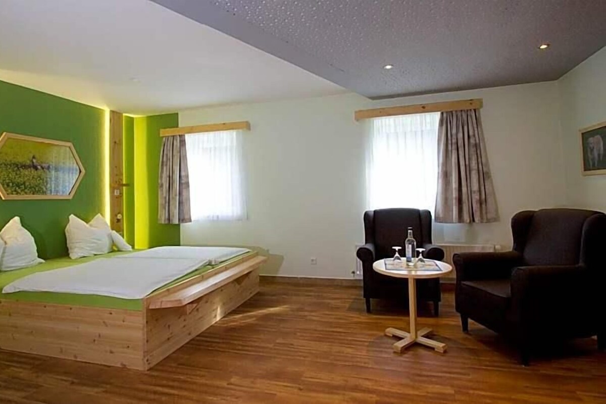 A room with a bed, two chairs, a small table, and a window with curtains.