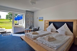 Habitación de hotel con dos camas, cabecera de madera, una mesita y vista al exterior.