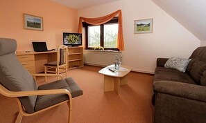 Una habitación con escritorio, laptop, televisor, sofá y ventana con cortinas.