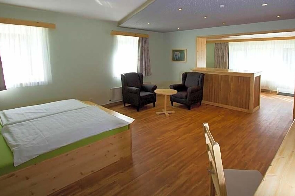 A room with a bed, two chairs, a small table, and a wooden desk.