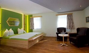 A room with a bed, two chairs, a small table, and a window with curtains.