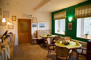 A dining area with a wooden table set for four, surrounded by chairs. There is a bench in the corner, a door, and framed pictures on the walls.