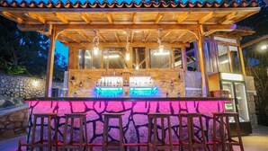 An outdoor bar area with wooden bar stools, a stone wall, and a tiled roof. - Mira Suites (Bodrum)