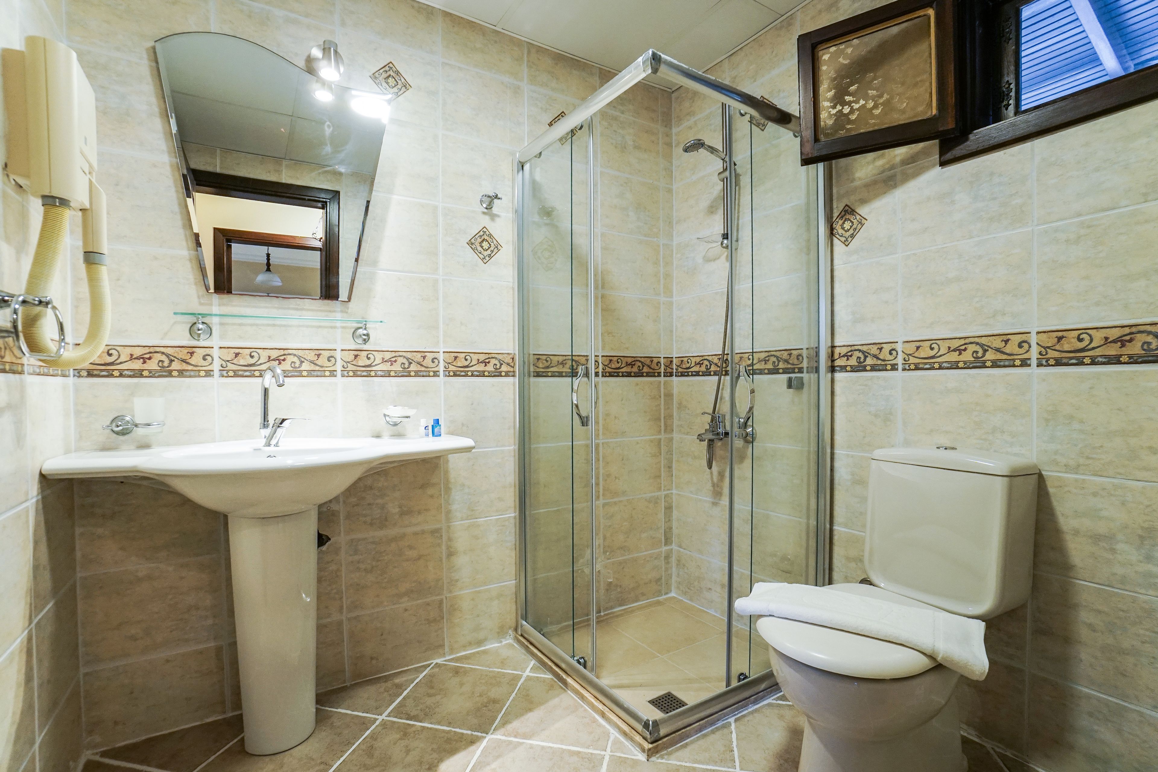 Un baño con ducha de vidrio, lavamanos pedestal y un inodoro.