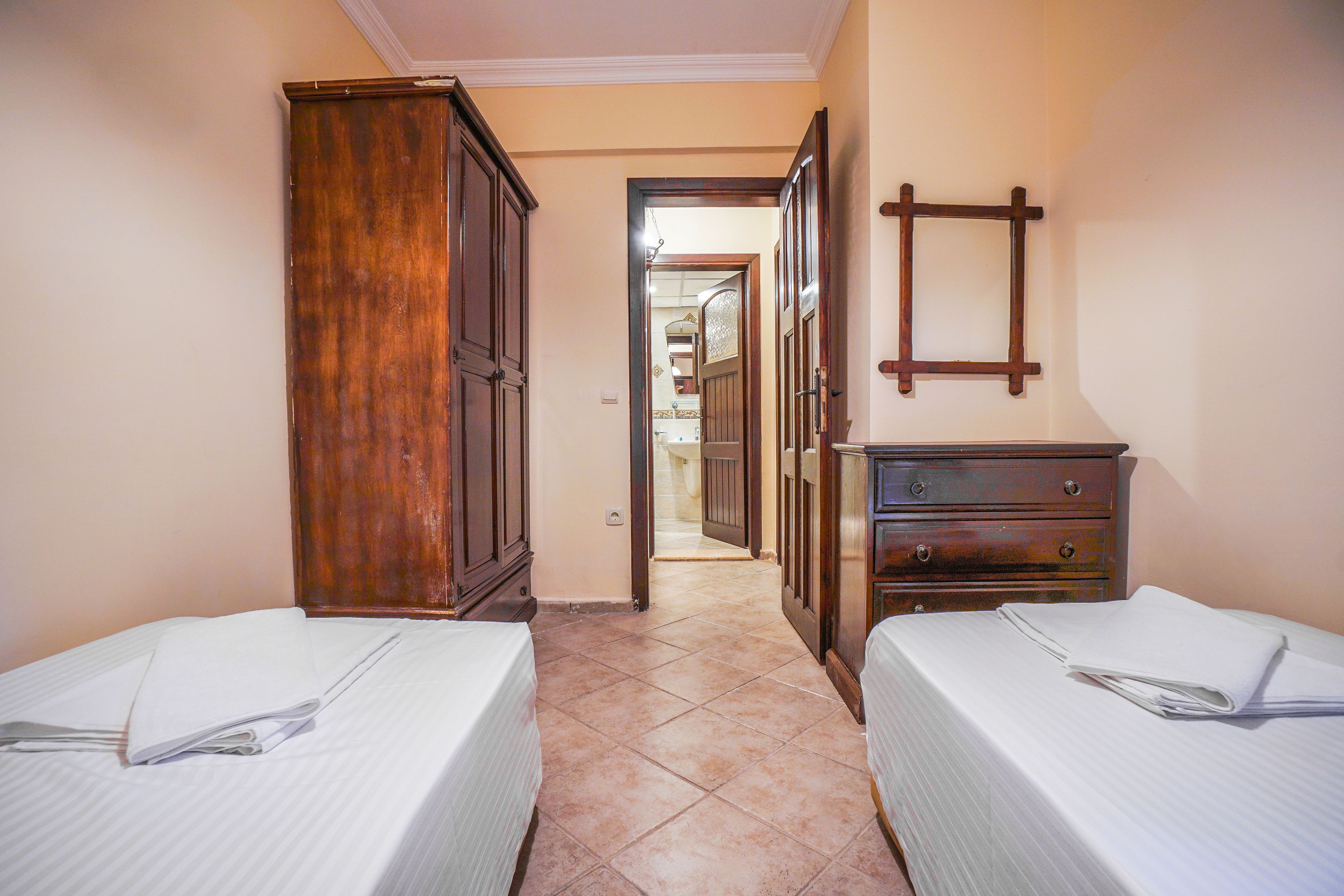 A hotel room with two beds, a wooden wardrobe, a dresser, and a mirror on the wall.