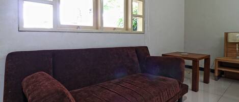 A room with a dark brown sofa, a small wooden table, and a window with blinds.