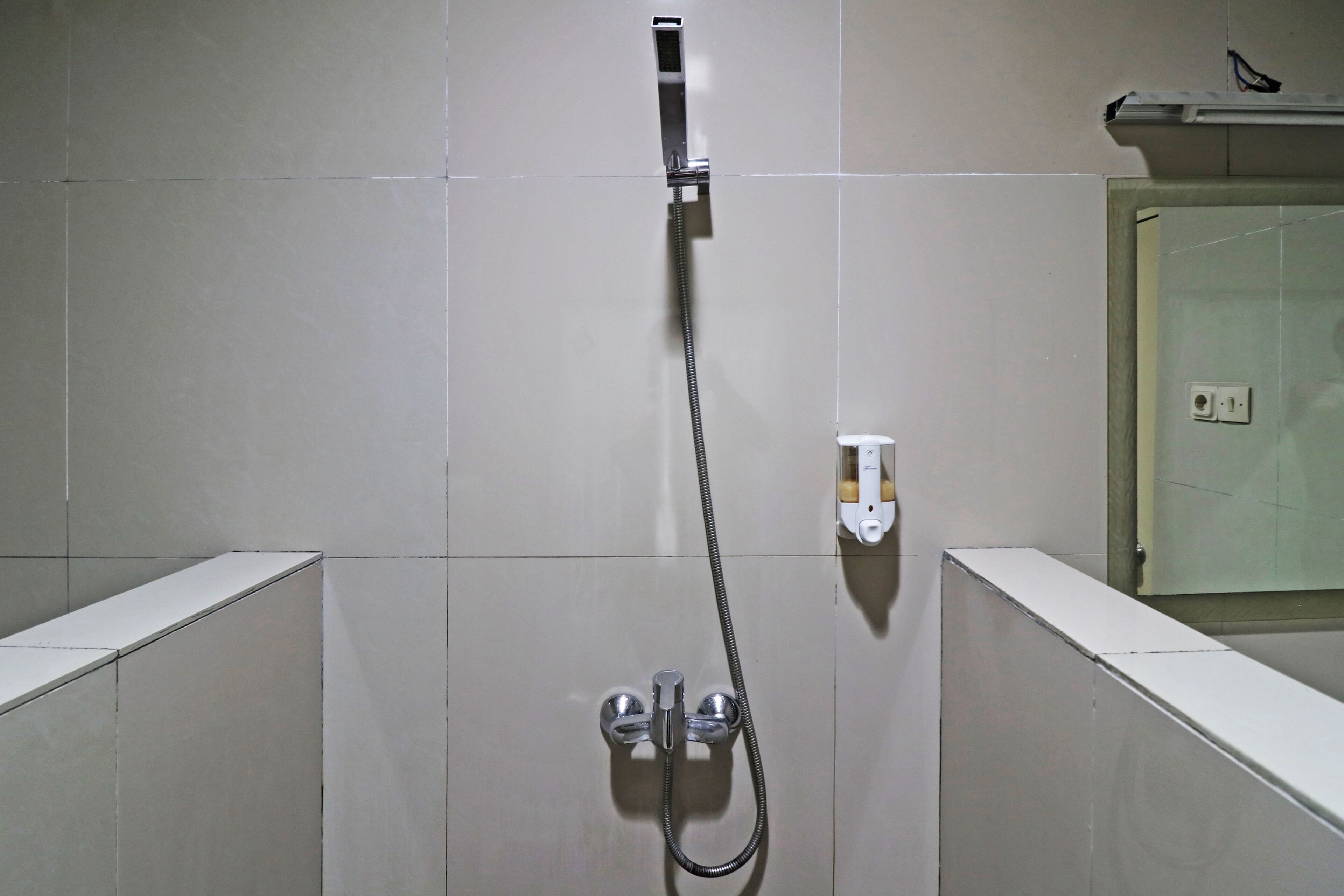 Ducha con manguera de mano, grifo empotrado en la pared y toma de corriente.