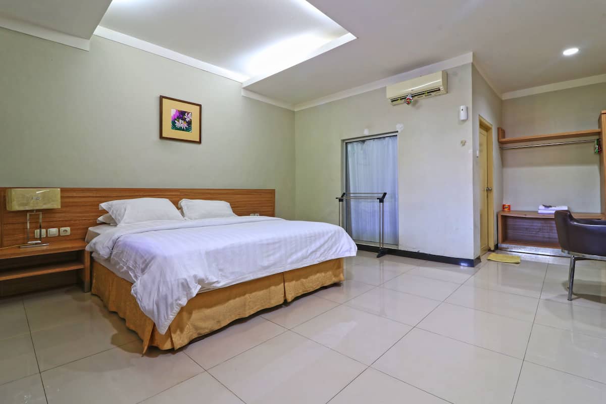Quarto de hotel com cama, escrivaninha, cadeira, janela e porta.
