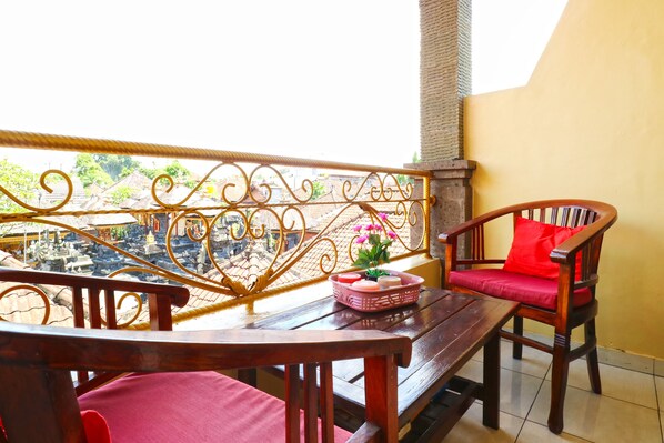 A balcony with a wrought iron railing, a wooden table, and two wooden chairs with red cushions.