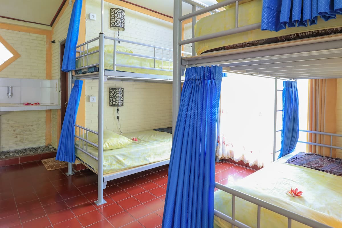 A dormitory room with bunk beds, a window with blue curtains, a white sink, and a tiled floor.