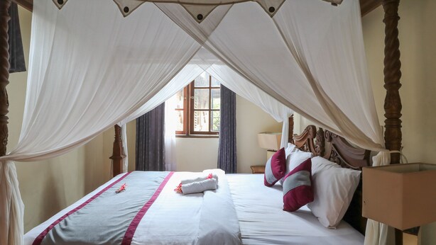 A neatly made bed with white and pink bedding, a canopy, and a bedside table with a lamp. - Ubud Asri Homestay (Ubud)