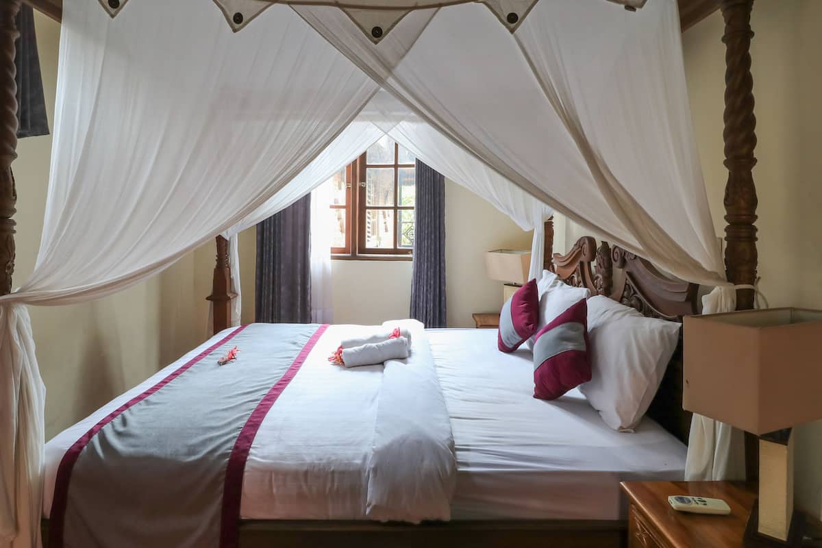 A neatly made bed with white and pink bedding, a canopy, and a bedside table with a lamp.