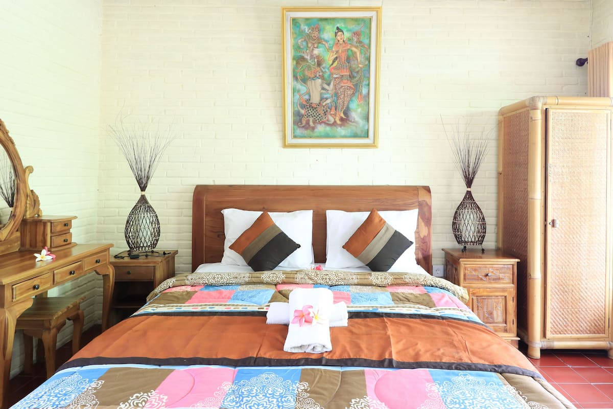 A neatly arranged hotel room with a large bed, a wooden headboard, a painting on the wall, and a wardrobe.