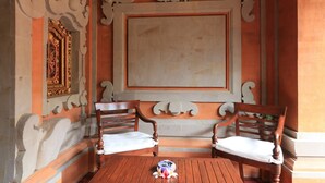 A room with two wooden chairs and a table, ornate wall decorations, and a large framed artwork. - Ubud Asri Homestay (Ubud)