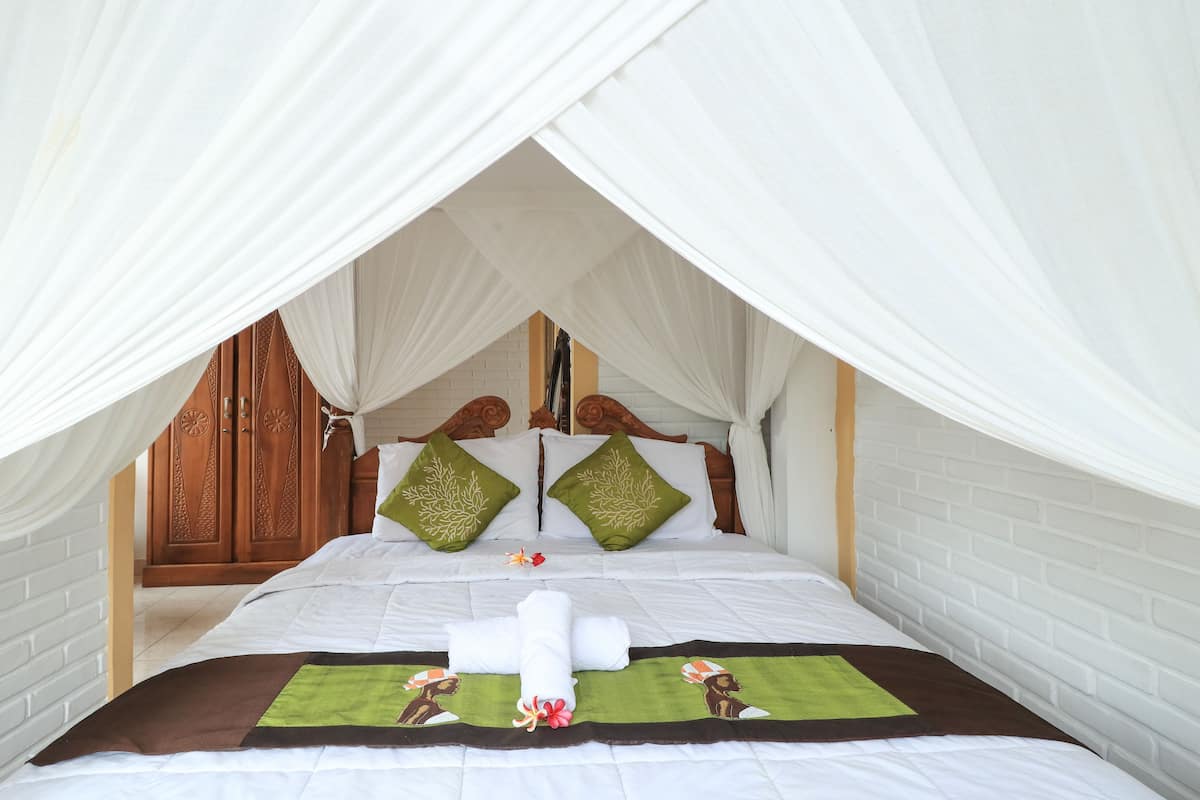 A bed with a canopy, two green pillows, a white bedspread, and a brown and green blanket.