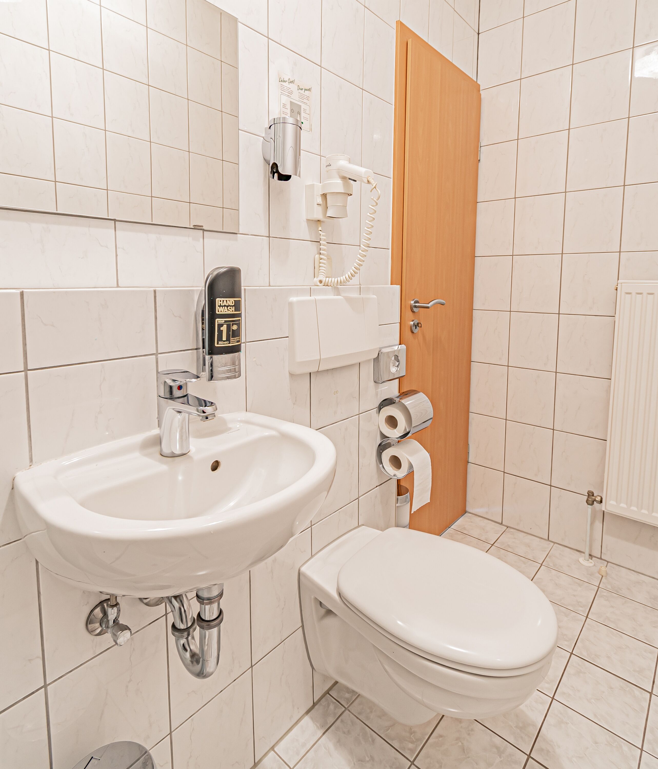 Une salle de bain équipée d’un lavabo, de toilettes, d’un sèche-mains et d’un distributeur de serviettes en papier.