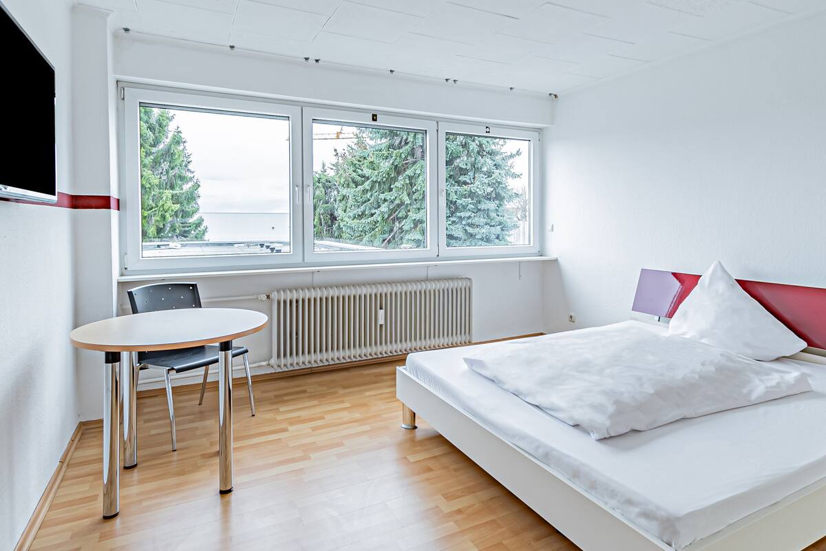 Quarto moderno com uma cama, uma mesa e duas janelas.
