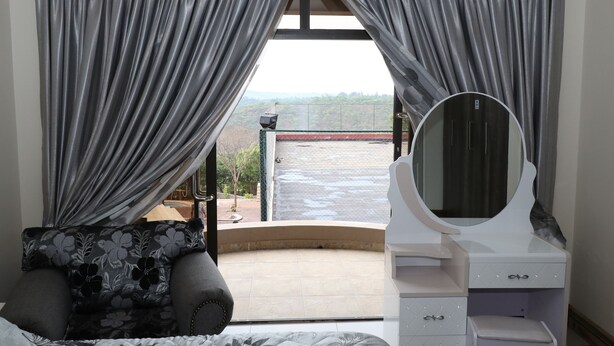 A room with a balcony, a bed, a vanity with a mirror, and grey curtains. - Shiloh Luxury Lodge (Harare)
