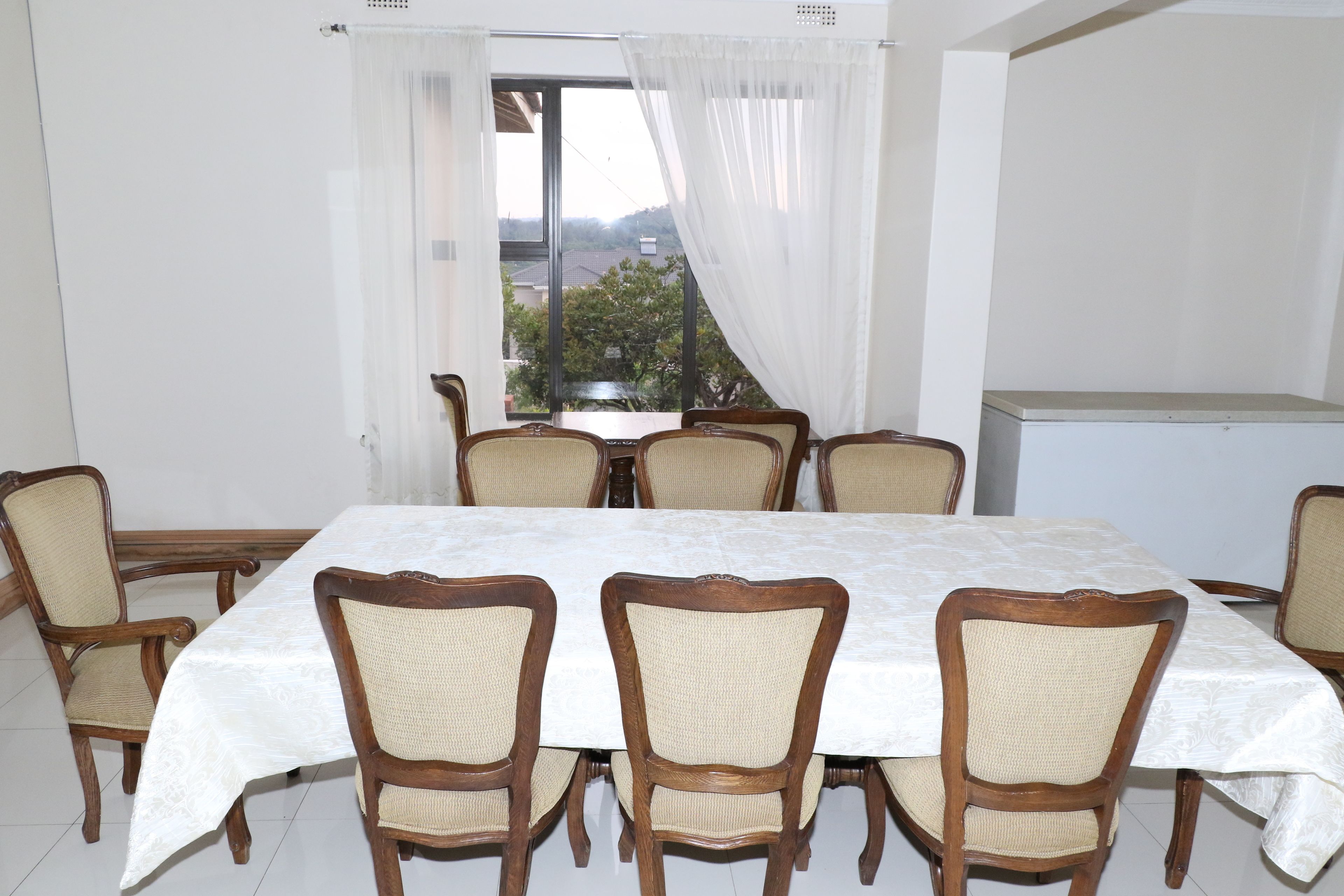 A dining area with a table and chairs, a window with curtains, and a view of the outside.