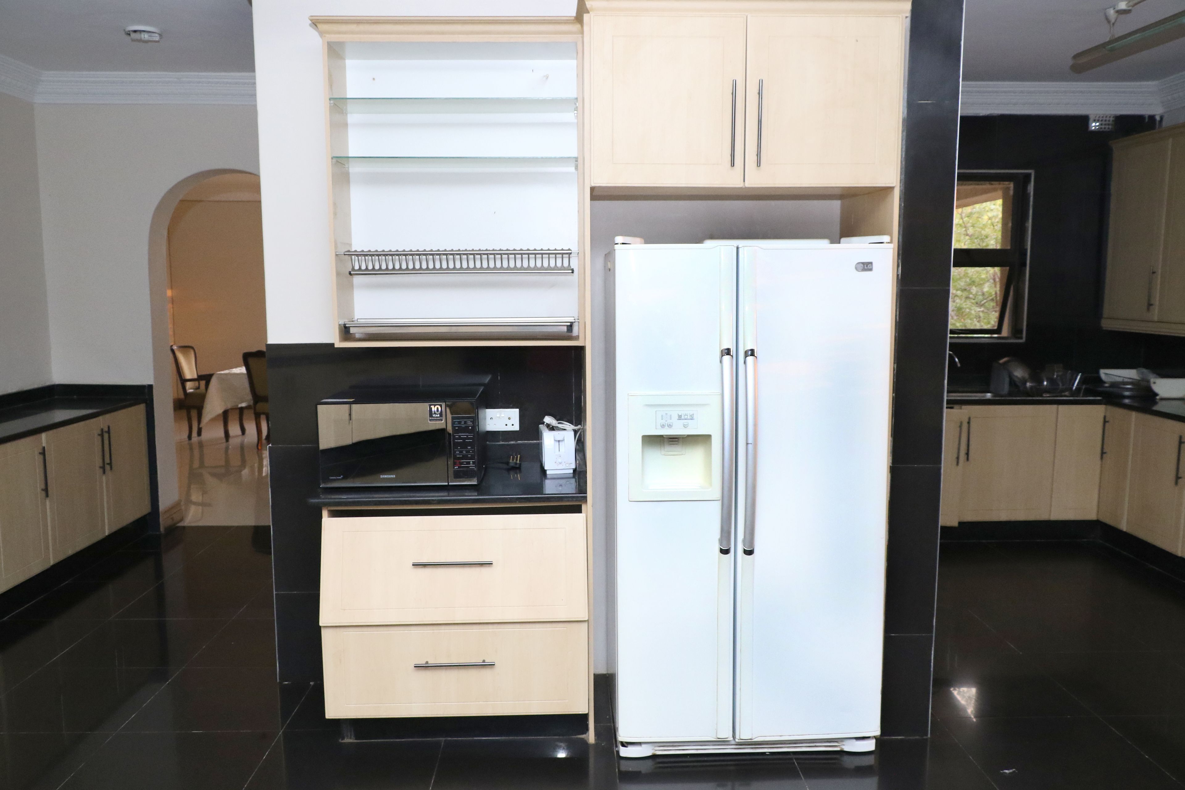 Een moderne keuken met een witte koelkast, beige kastjes en een zwart aanrecht.