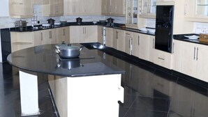 A modern kitchen with light wood cabinets, a black countertop, and a central island with a stove. - Shiloh Luxury Lodge (Harare)