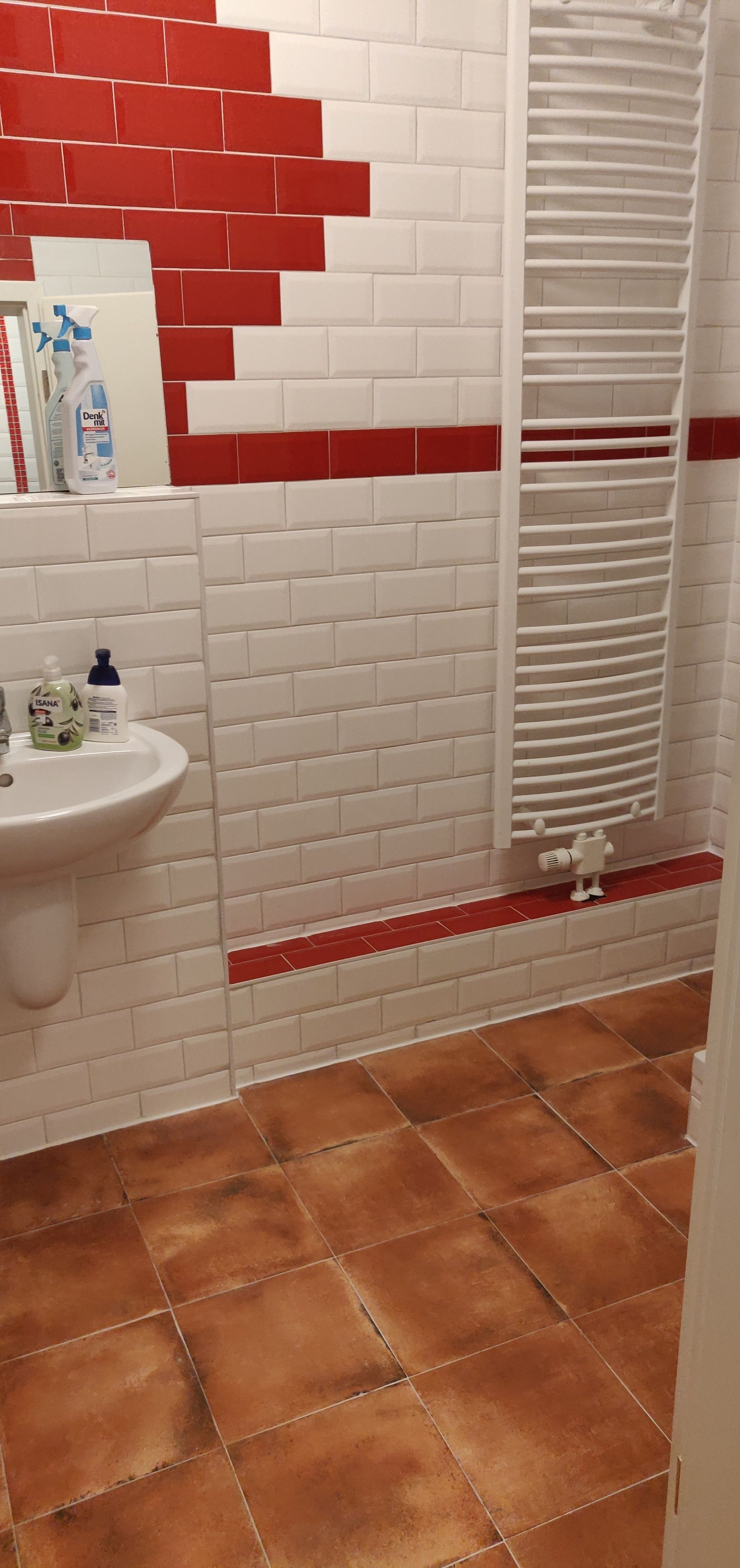 A bathroom with white and red tiled walls, a white sink, and a towel rack.