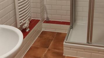 A bathroom with white and red-tiled walls, a white sink, and a glass shower enclosure.